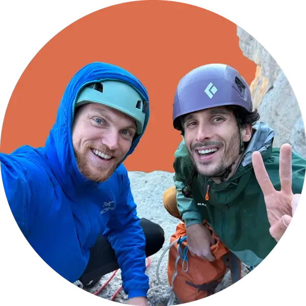 Charlie and a climbing partner grinning at the camera on a snowy col, one of them flashing a peace sign.