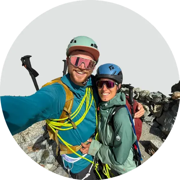 Charlie and Carmen on a summit in sunglasses and harnesses, the glacier behind them.