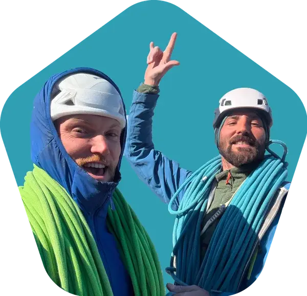 Two climbers with ropes coiled over their shoulders, one throwing a hand up to the camera.