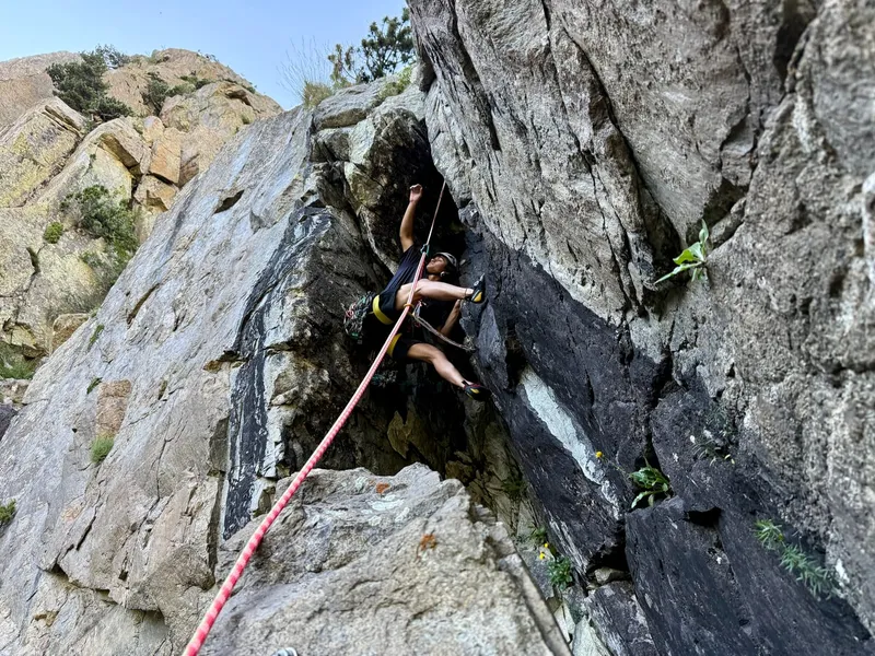 A climber bridging a granite groove in Aigüestortes, weathered granite domes standing behind.