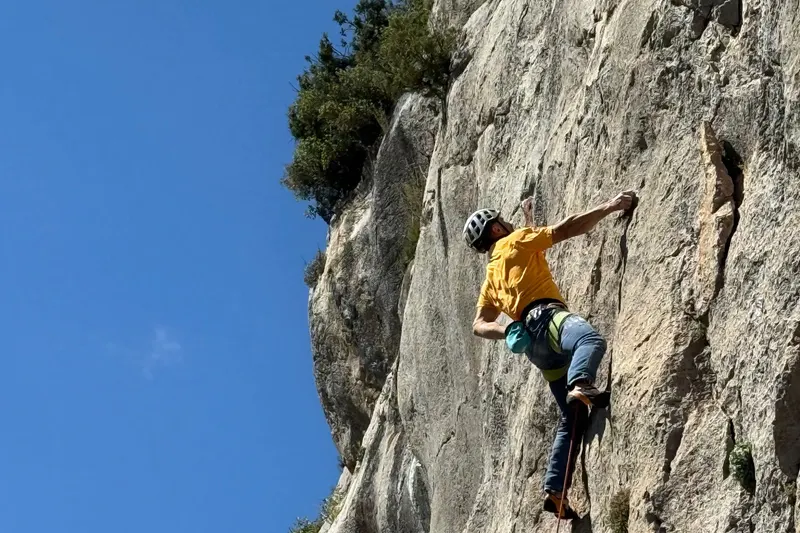 a climber leading a steep grey limestone wall, the rope running down below them.