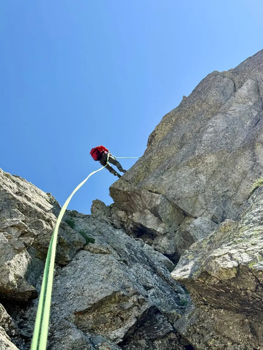 A climber moving along a rocky ridge, the rope running back down the crest.