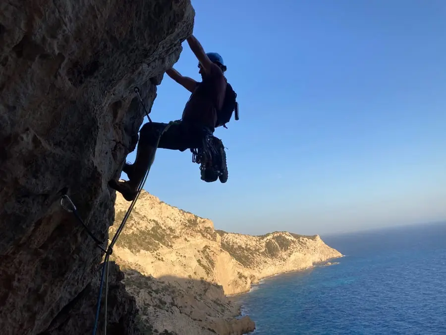 A climber high on a sea cliff, the Mediterranean flat and blue below.
