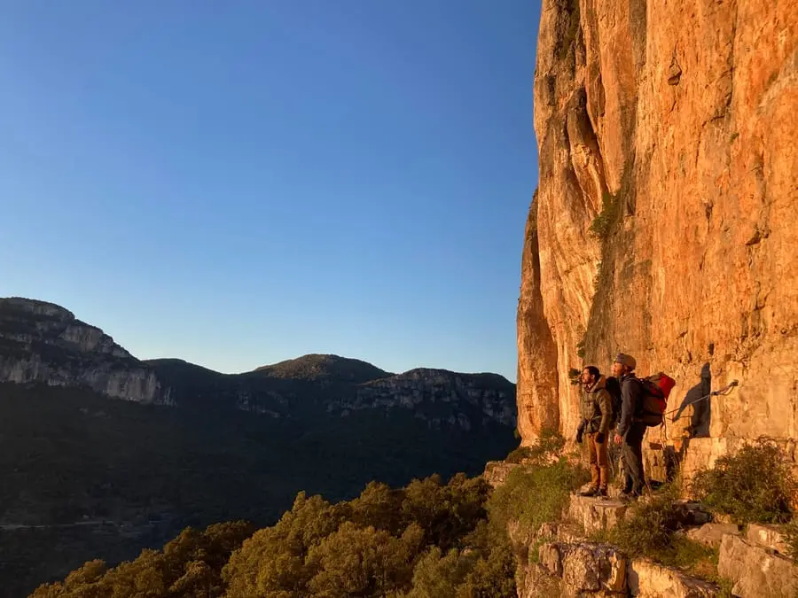 A big orange limestone wall catching the last of the sun, climbers small at its foot.