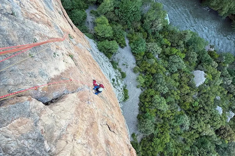a climber at a belay stance partway up a route, the river far below.