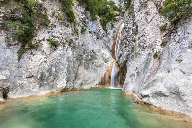 The Salt del Brull in the Sant Aniol gorge above Sadernes, a waterfall dropping between pale limestone walls into a green pool.