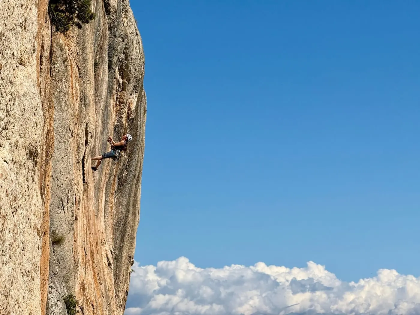 A climber high on a steep orange limestone wall, with cloud sitting in the valley far below.