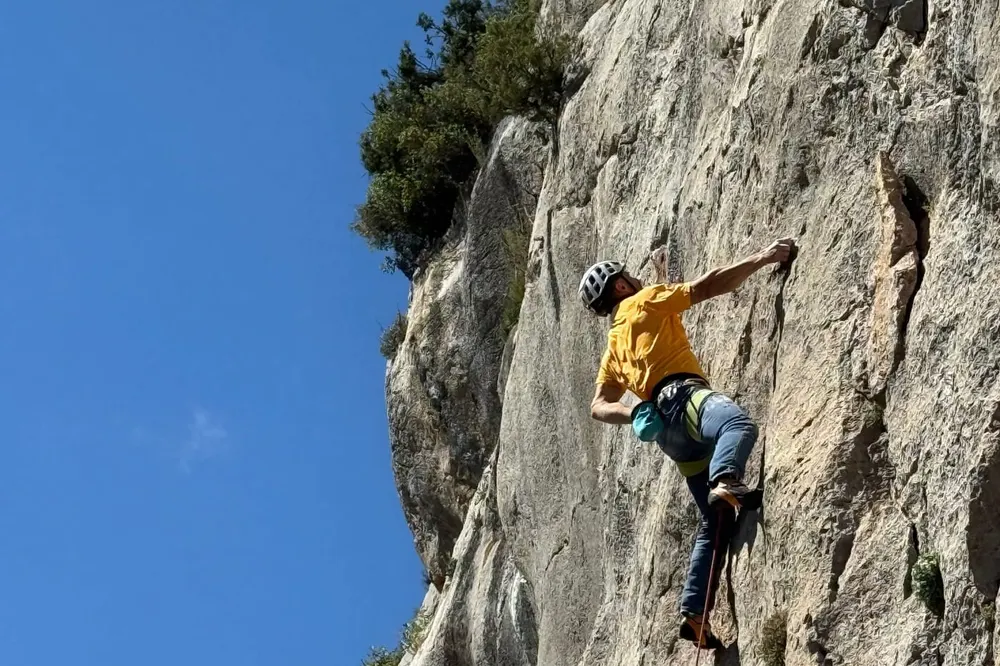 A climber in a yellow T-shirt leading a steep grey limestone wall, the rope running down below them.