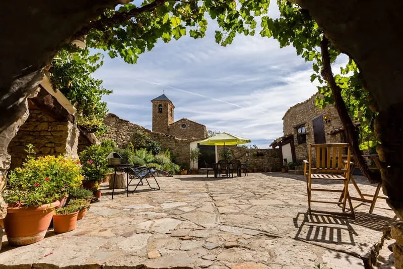 The shared courtyard under a vine, with the village church tower behind it.
