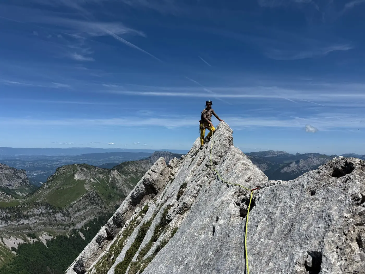 A climber standing on the limestone crest of the Urquiza-Olmo ridge, rope trailing, the ranges falling away behind under a blue sky.